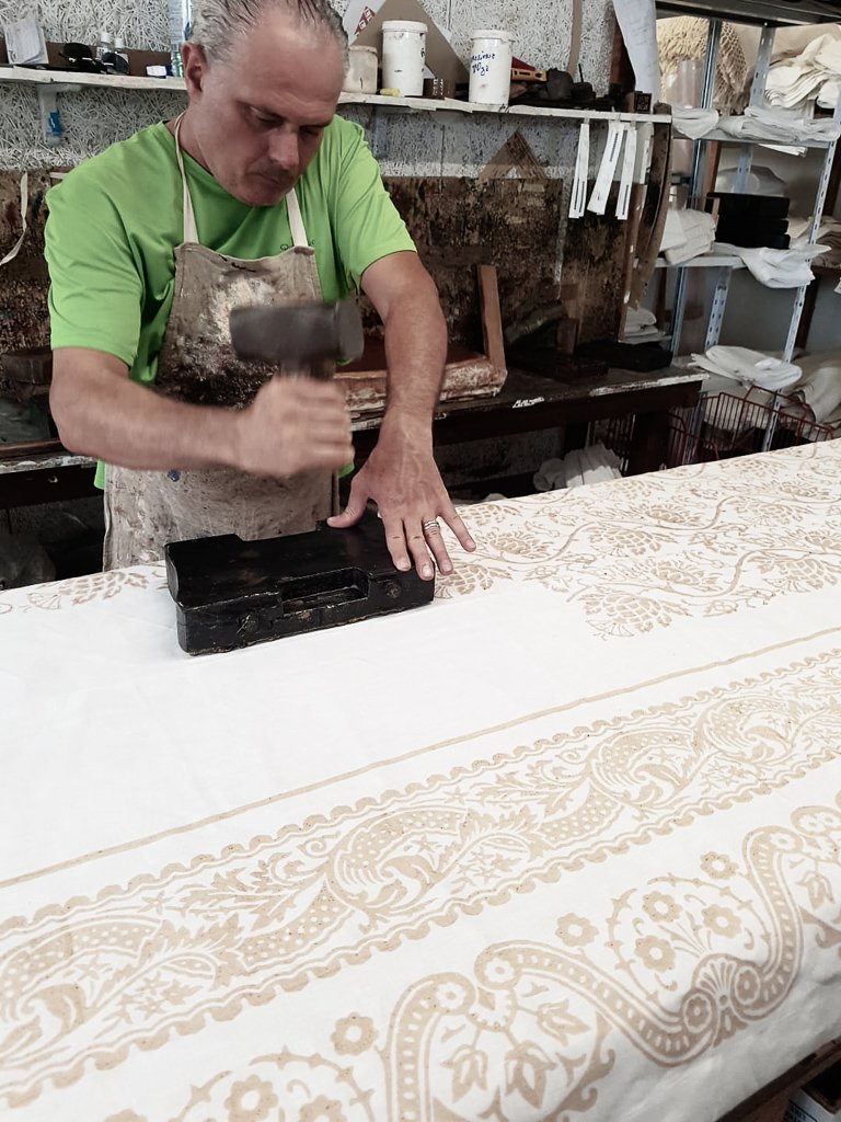 Linen tablecloth in the process of being block-printed. A man is hammering a block of pear wood