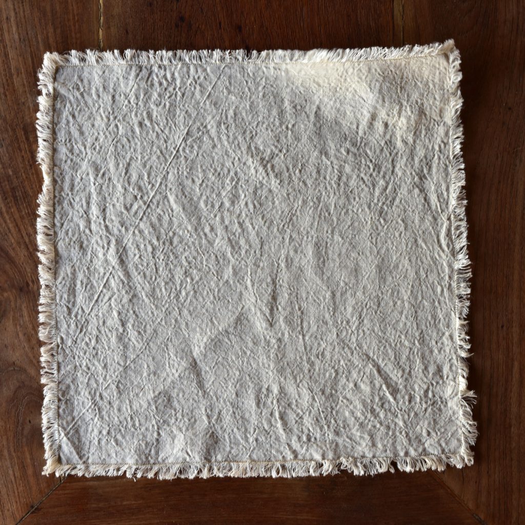 hemp napkin (dark cream) - hemp linen napkin with fringes - image displays napkin laid out on wooden floor