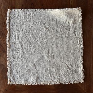 hemp napkin (dark cream) - hemp linen napkin with fringes - image displays napkin laid out on wooden floor