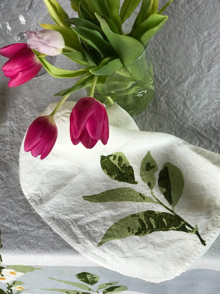 Folded Camellia linen napkin rests in front of a vase filled with tulips.