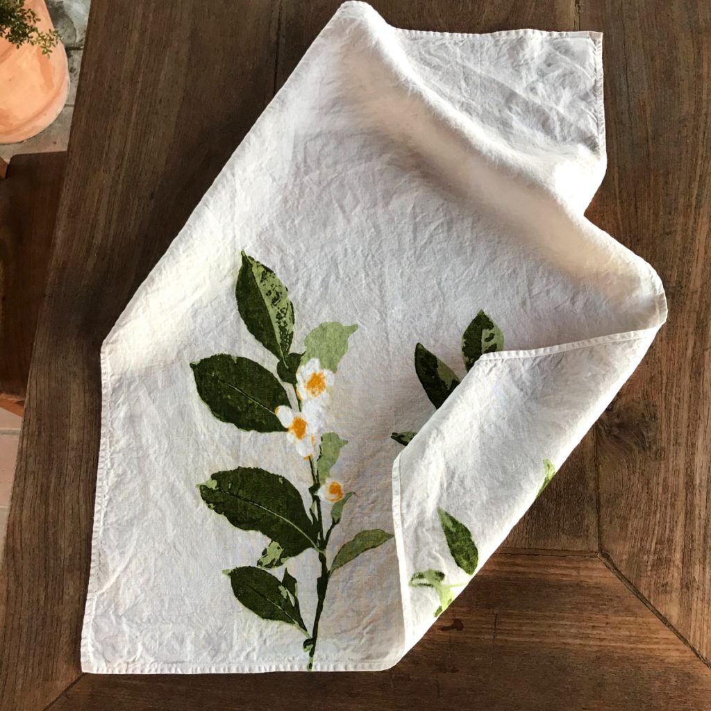 Shot from above of the Camellia organic linen tea towel. The tea towel is folded up at the corner to further display its detailing.