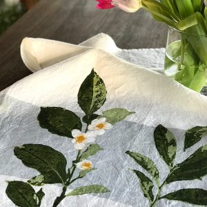 Close-up detailing of the motifs of the Camellia organic linen tea towel with band. A vase containing tulips sits atop the tea towel, to the upper right-hand side of the image.
