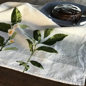 Close-up detailing of the motifs of the Camellia organic linen tea towel with band. Atop the tea towel rests a plate, upon which sits a chocolate cake and fork.