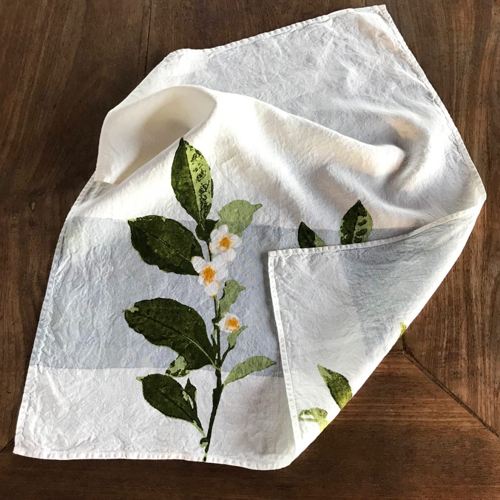 Close-up detailing of the motifs of the Camellia organic linen tea towel with band. The tea towel is folded up at the corner to further display its embellishments.