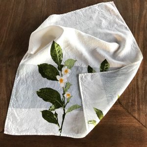 Close-up detailing of the motifs of the Camellia organic linen tea towel with band. The tea towel is folded up at the corner to further display its embellishments.