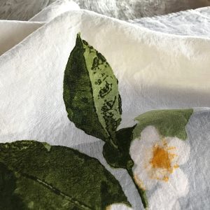 Close-up detailing of the motifs of the Camellia organic linen tea towel with band.