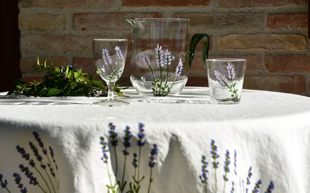 handblown murano glass glassware in lavender motif laid on a natural linen tablecloth for a charming outdoor dinning setting