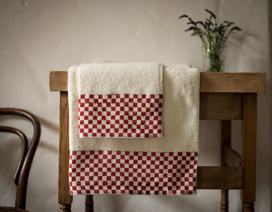 Two red and white cotton towels draped over the edge of a wooden table