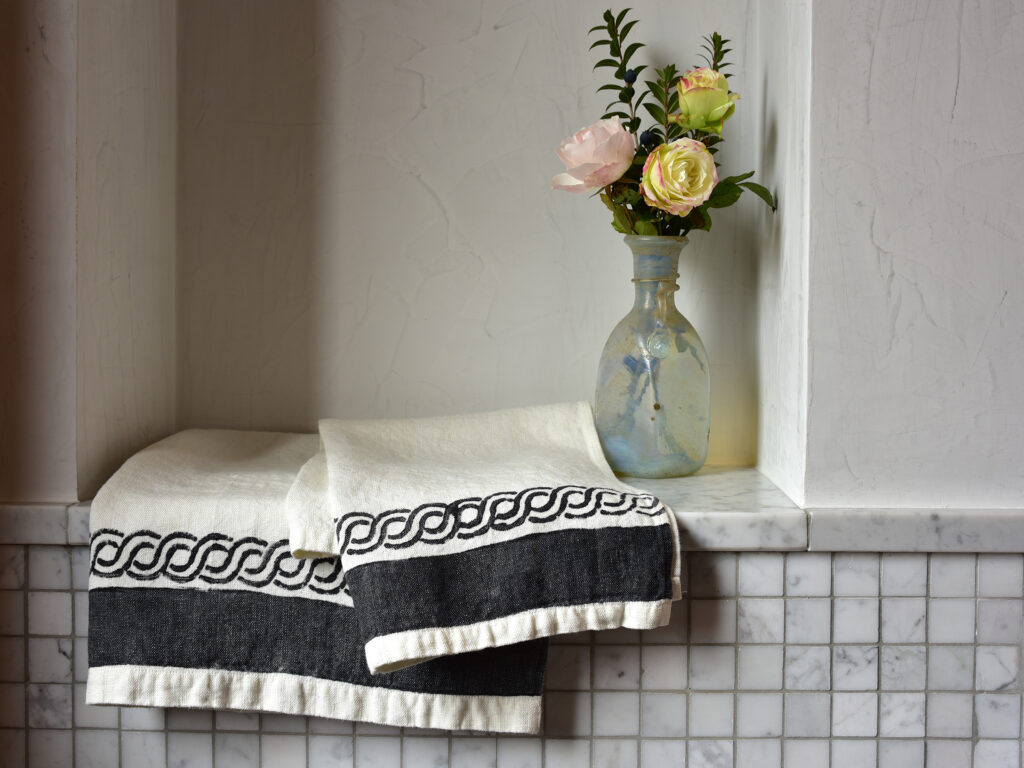 Two white and grey towels folded on a tiled surface next to a vase of flowers
