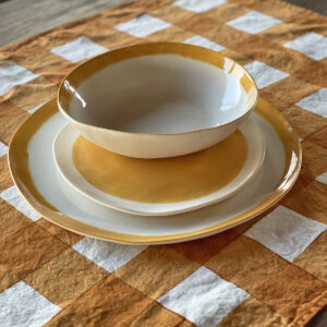 hand painted mustard porcelain dinner set displayed on a linen checked placemat