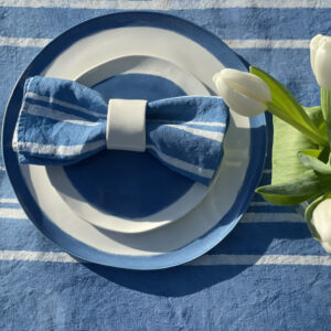 Hand painted linen napkins and porcelain dinnerware set on a blue linen tablecloth and flower