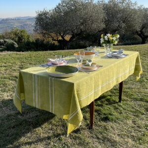 A green linen tablecloth with white stripes on a laid table in a garden. Flowers are also on the table.