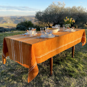 A mustard linen tablecloth with white stripes on a laid table in a garden. Flowers are also on the table.