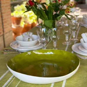 A green porcelain serving bowl on a table set with a green tablecloth, glasses and a vase of flowers