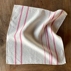 A white linen napkin with pink stripes laid out on a wooden table
