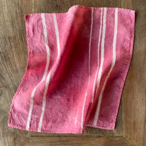A pink linen napkin with white stripes laid out on a wooden table