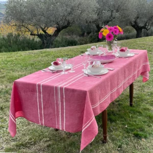 A pink tablecloth with white stripes on a laid table in a garden. Flowers are also on the table.