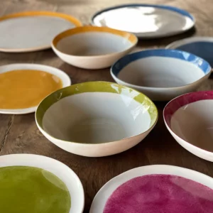 An array of white, pink, blue, green and orange porcelain dishes of varying sizes on a wooden table