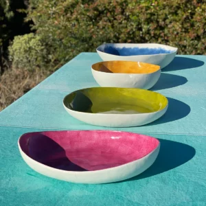 Pink, green, yellow and blue porcelain serving bowls lined up on top of a turquoise tablecloth