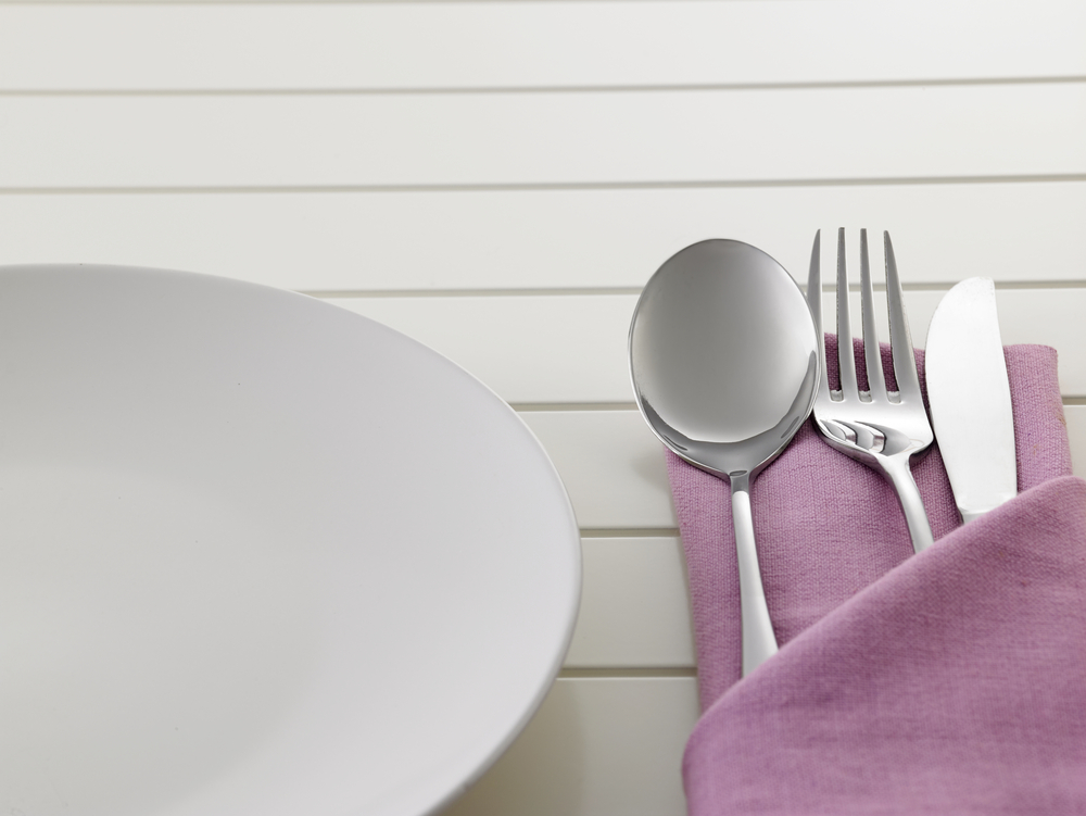 A folded purple linen napkin holding cutlery next to a plate