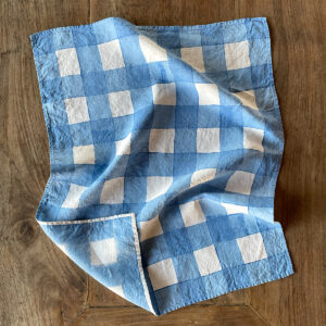 Blue hand-painted checked linen tea towel laid on a wooden table