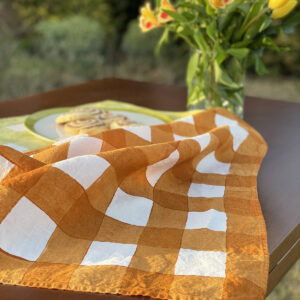 Checked tea towel laid on table with a handmade biscuits and a vase of flowers on the side