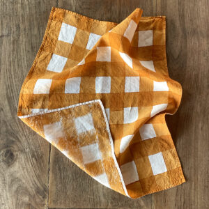 Mustard hand-painted checked linen tea towel laid on a wooden table