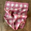 Pink hand-painted checked linen tea towel laid on a wooden table