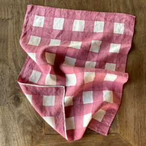Pink hand-painted checked linen tea towel laid on a wooden table
