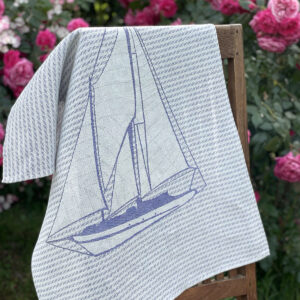 Nautical blue italian jacquard kitchen towel laid on a chair with flowers in the background