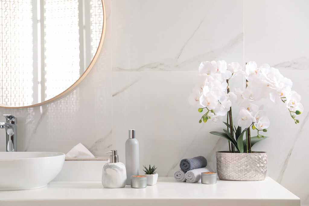 stylish and modern spa-like bathroom with beautiful flowers, burning candles and different toiletries on countertop