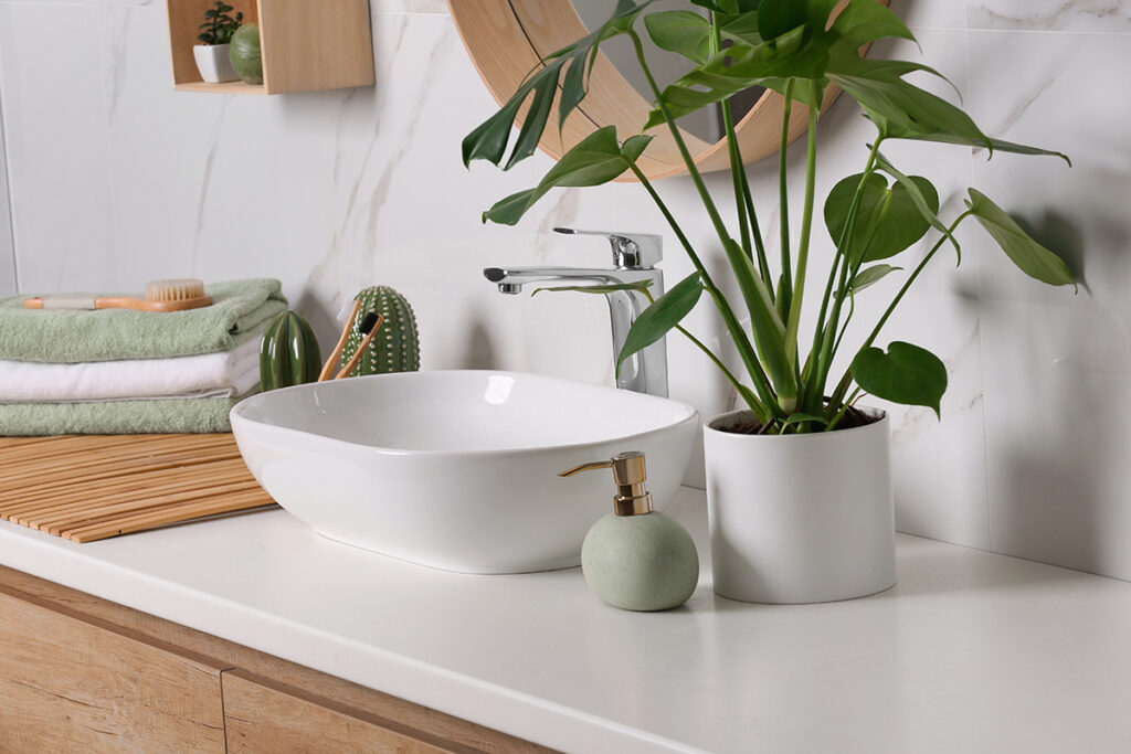 Stylish vessel sink on light countertop in modern bathroom with plants
