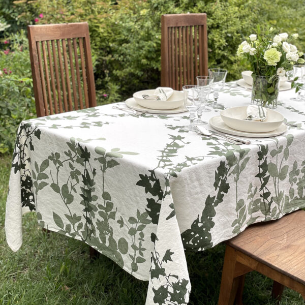 hand-printed botanical linen tablecloth laid on a wooden table in a garden with roses in the background