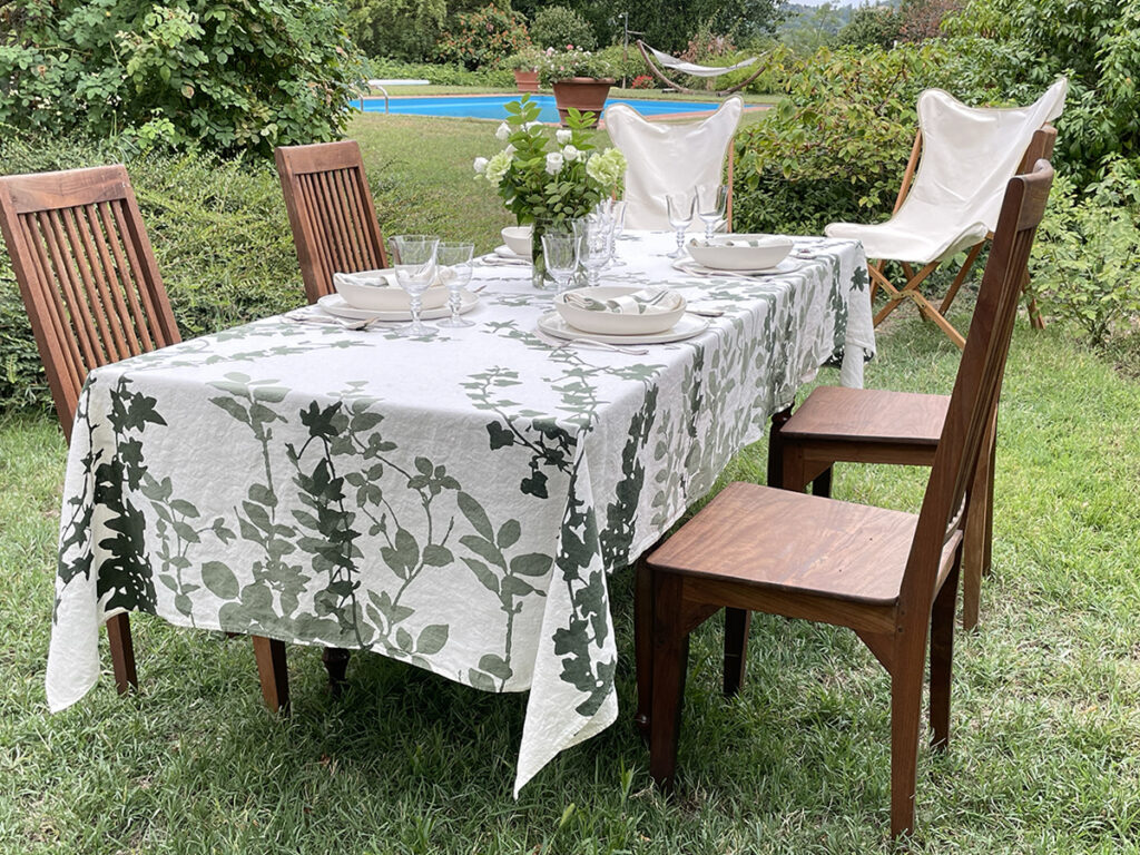 alfresco table setting arranged in the garden with floral linen tablecloth and a swimming pool in the background