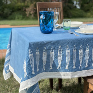 Hand-painted seaside style tablecloth laid by a pool with blu murano jug and porcelain dinnerware on top