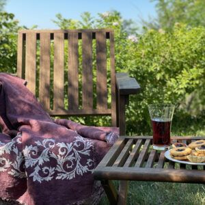 linen throw laid on a wooden chair in the outdoor with a pomegranate juice an biscuits on the side table