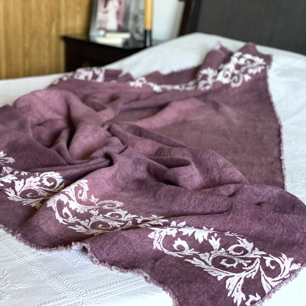 hand-pinted plum linen throw laid on bed with a bedside table on the background