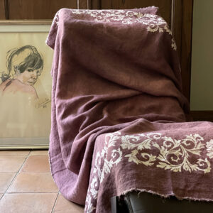 linen throw in a plum colour laid on a lounge chair with a painting in the background