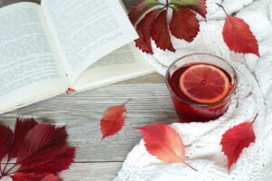 Autumn leaves, cup of herbal tea with lemon, warm blanket and open book on old wooden table. Rose hip and hibiscus tea. Seasonal, reading books, tea time, Sunday relaxing and still life concept.