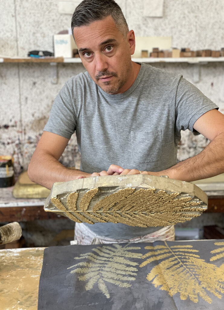 Italian artisan holding a wood-block to decorate a linen tablecloth in Palm design