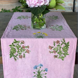 pink linen table runner laid across a wood table with a base of pink flowers sitting on top