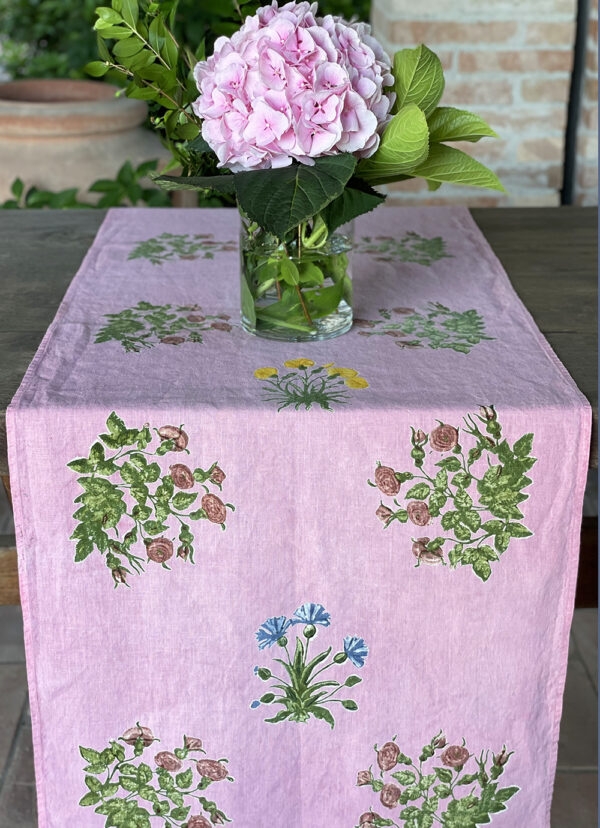 pink linen table runner laid across a wood table with a base of pink flowers sitting on top
