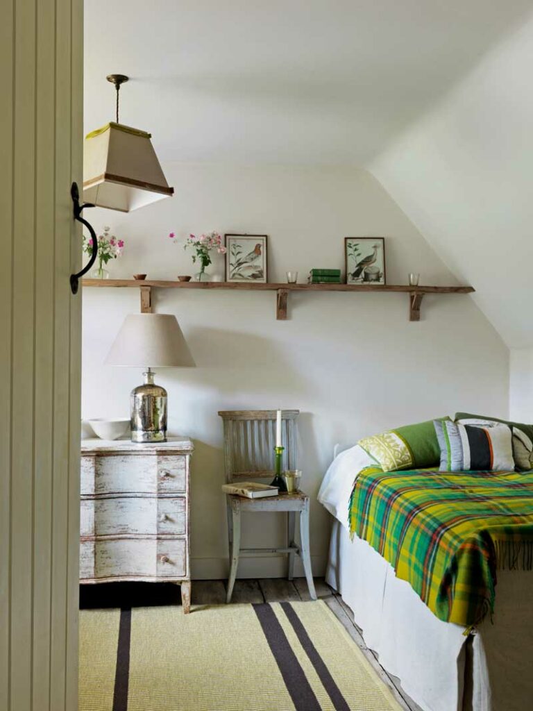 Farmhouse and cottage style bedroom with white walls, wooden furnitures and green patterned linens and cushions