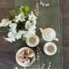 Hand-painted linen table runner in dark olive-green laid on a wooden table with ceramic crockery, flowers and biscuits