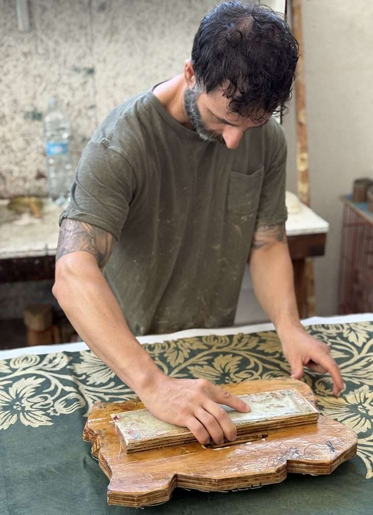 Italian craftsman block-printing a linen tablecloth with traditional design in gold colour