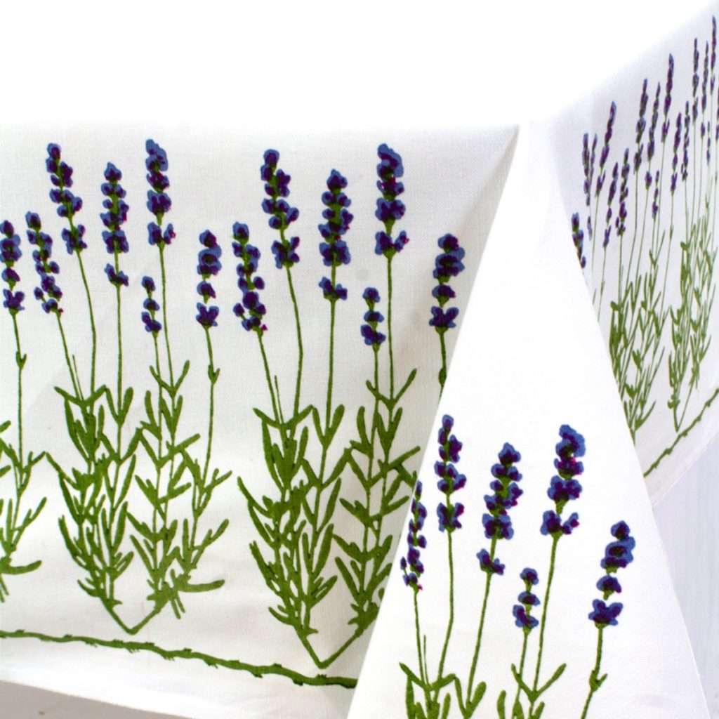 Overhead view of an AllÓRA natural flax linen tablecloth printed with a geometric repetition of slender lavender motifs, showing the deliberate plain spacing between prints on a long dining surface.