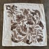 Block-printed brown linen napkin in damask design laid onto a wooden table