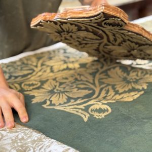 artisan block-printing a pomegranate motif in gold onto a green linen table runner