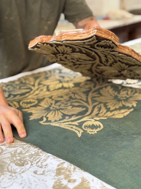 artisan block-printing a pomegranate motif in gold onto a green linen table runner